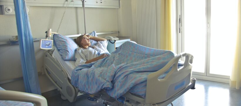 In einem Krankenzimmer im Krankenhaus liegt eine Patientin im Bett und schaut aus dem Fenster.
